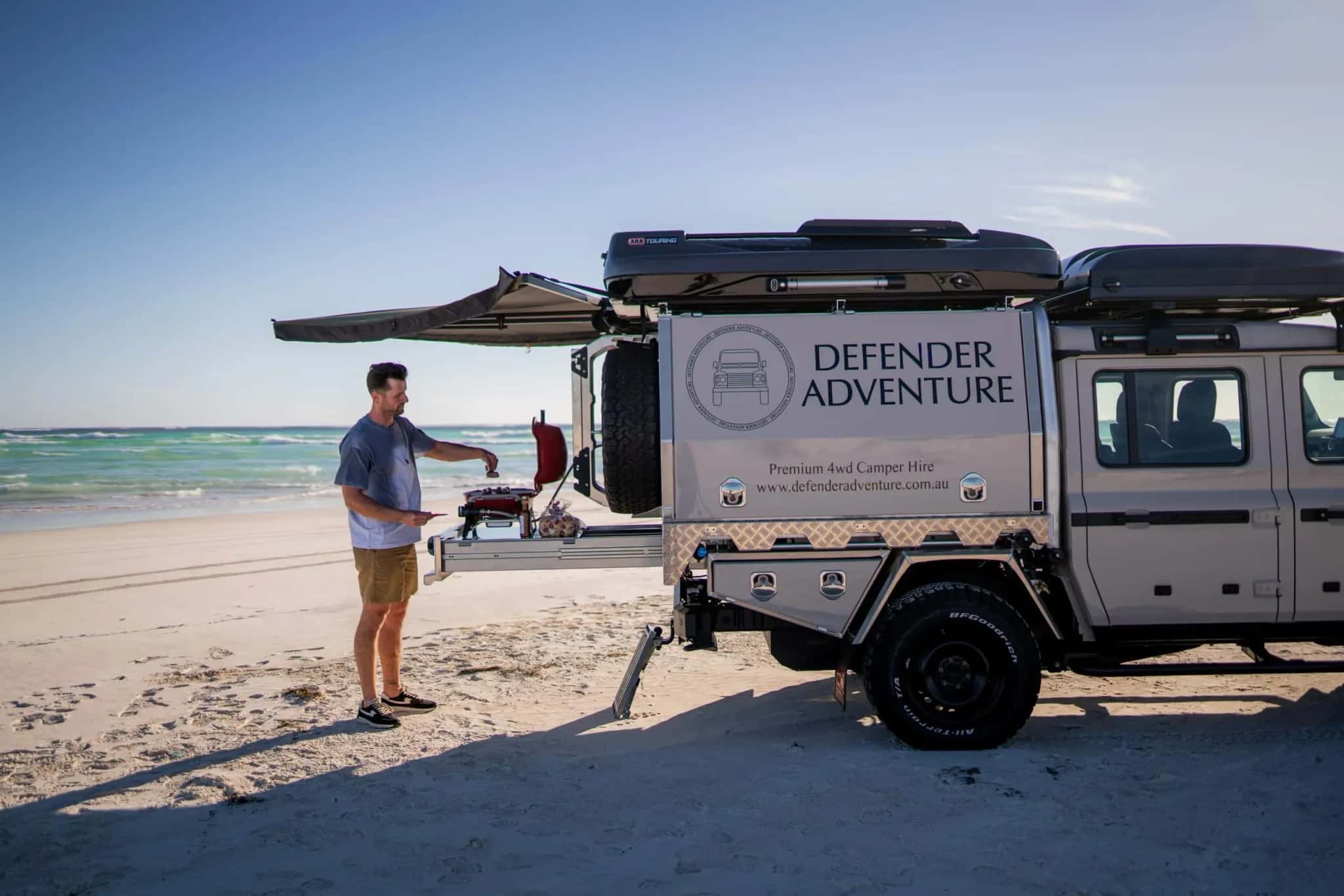 Defender Adventure 4WD Camper mit ausgefahrener Outdoor-Küche und Markise am Strand in Australien