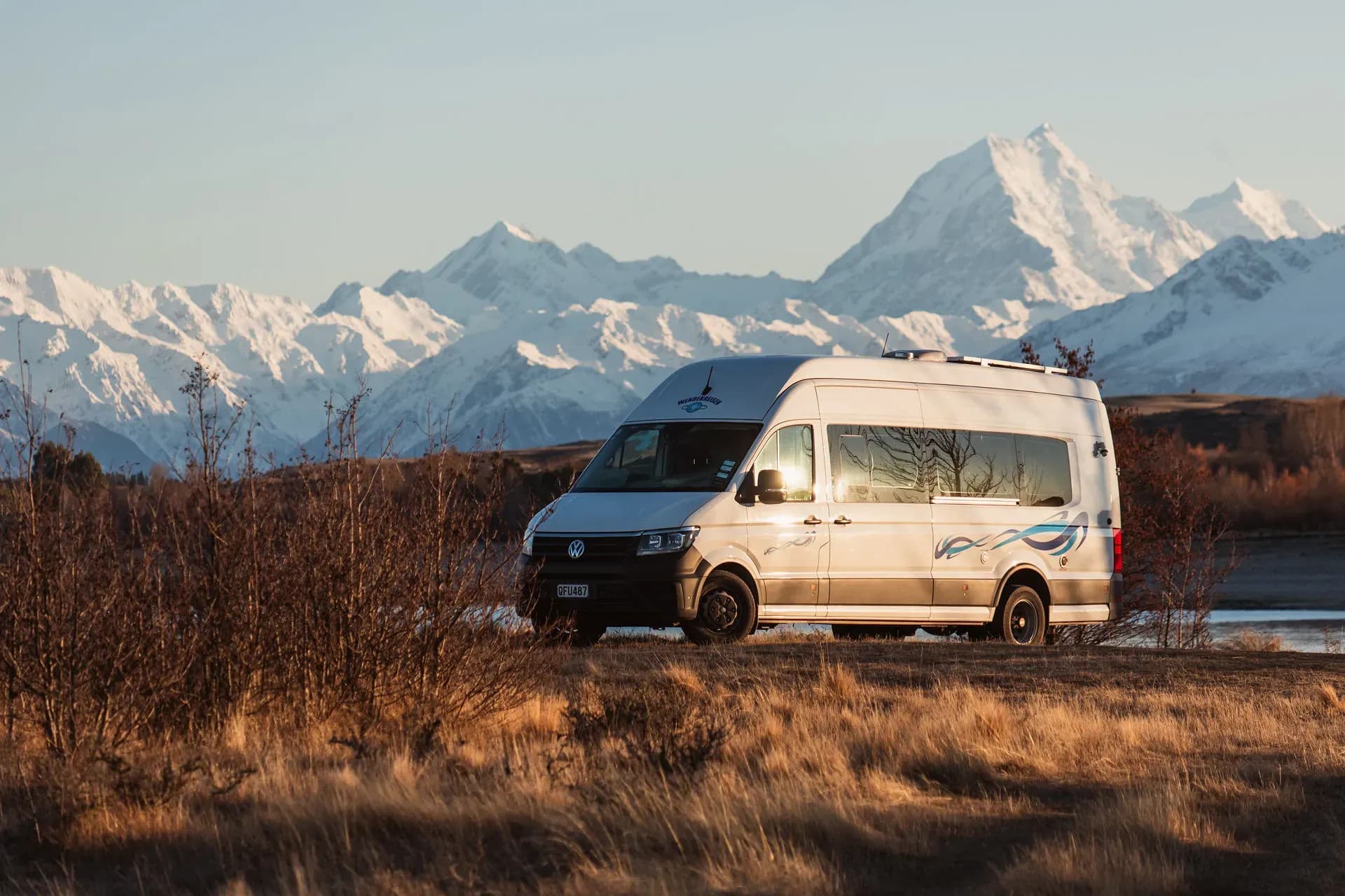 Wendekreisen Camper in Neuseeland vor schneebedeckten Bergen und goldener Landschaft.