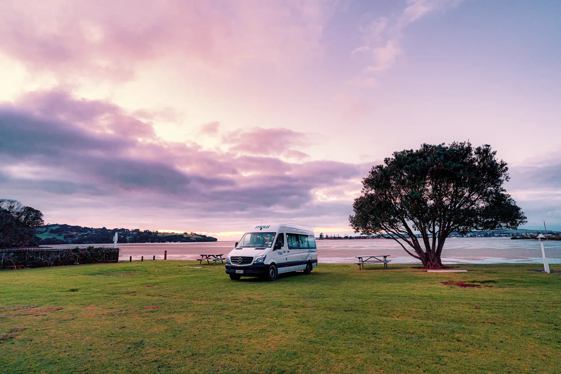 Ultima von Maui Motorhomes neben Baum vor See in Australien bei rötlichem Licht