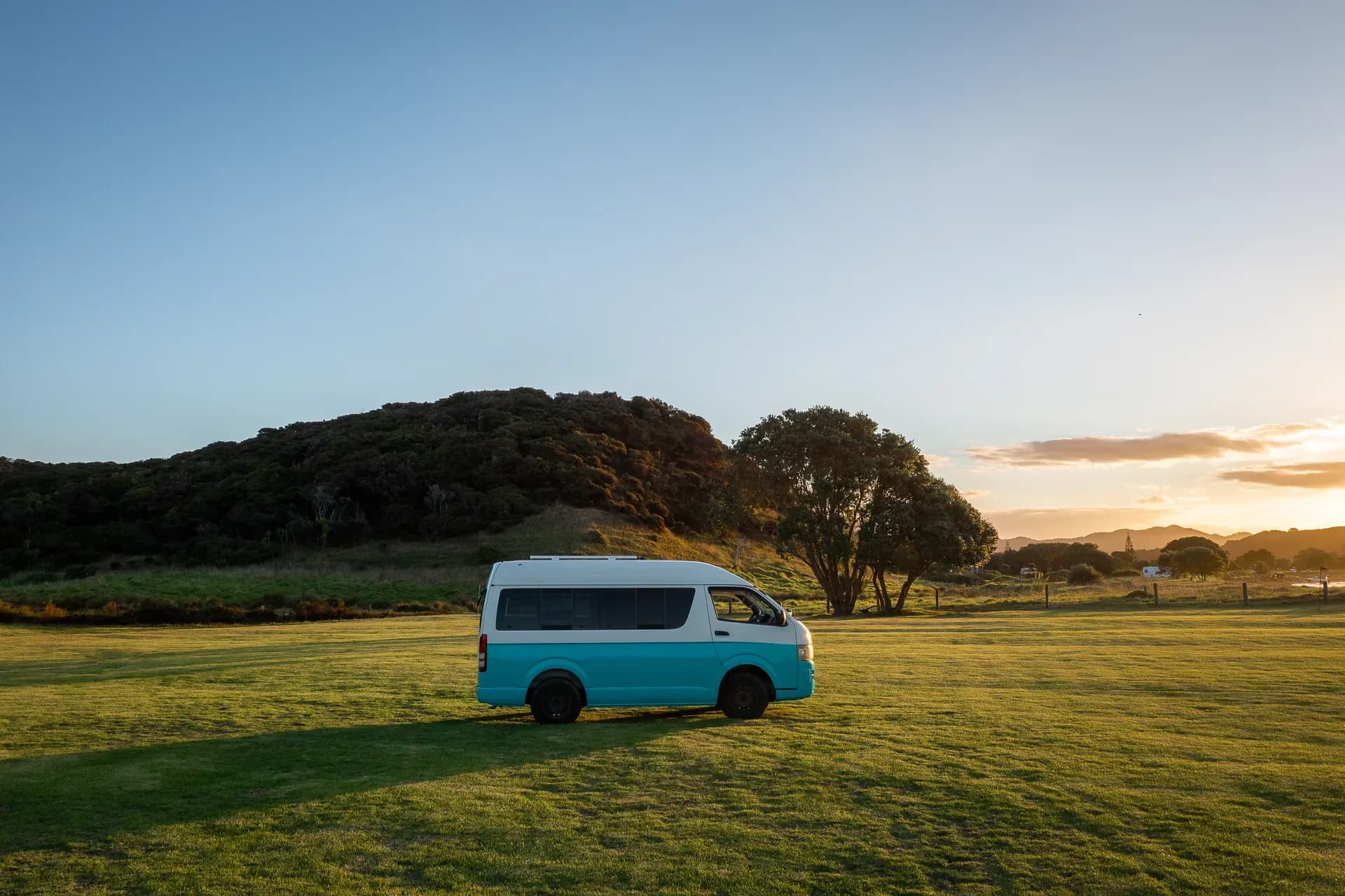 Der Willy Camper von Barefoot Camper in Neuseeland auf einer grünen Wiese.