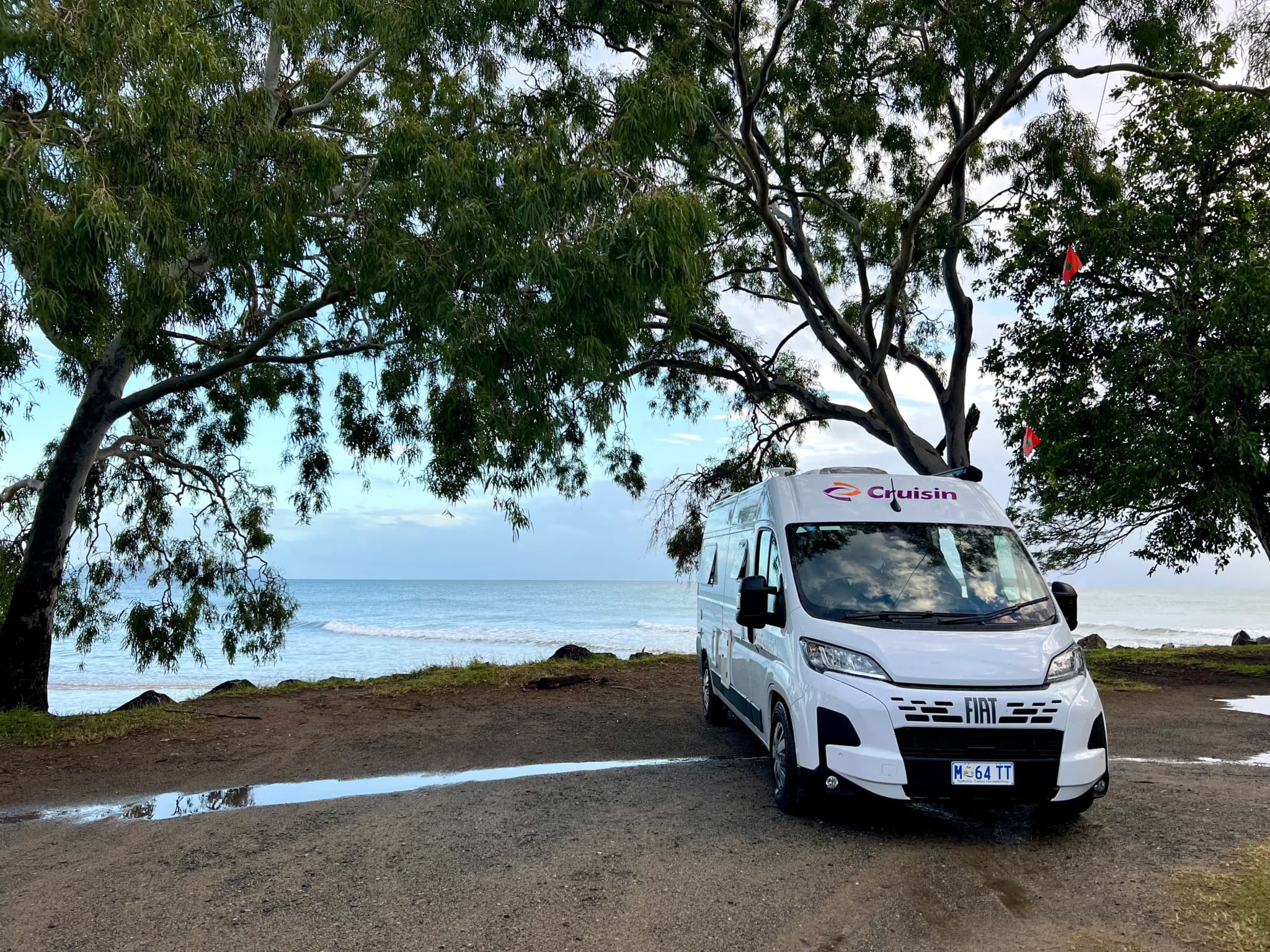 Camper unter Bäumen mit Meer im Hintergrund