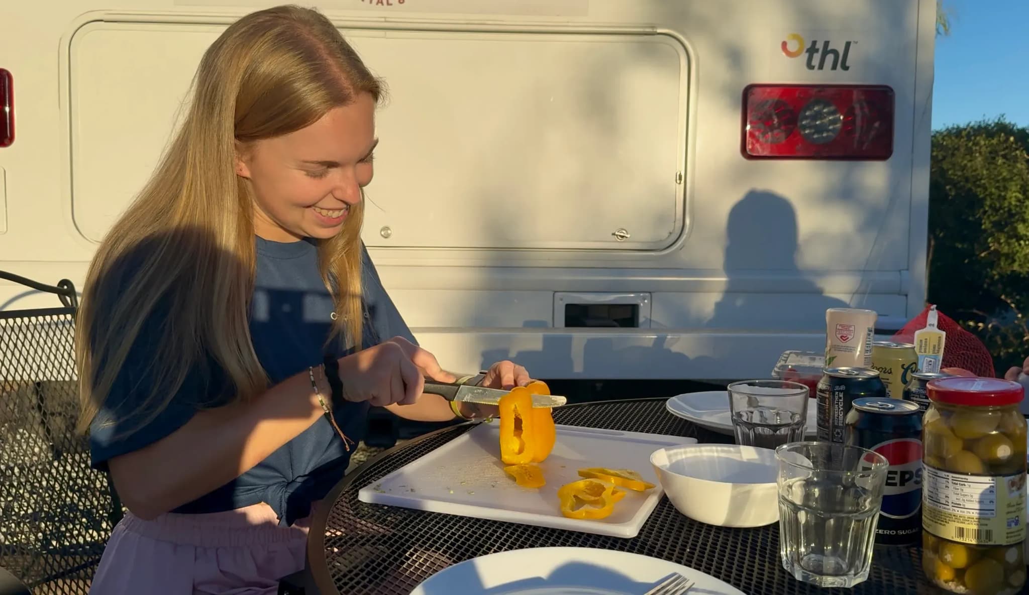 junge Dame am Paprika schneiden vor einem Camper im Sonnenlicht