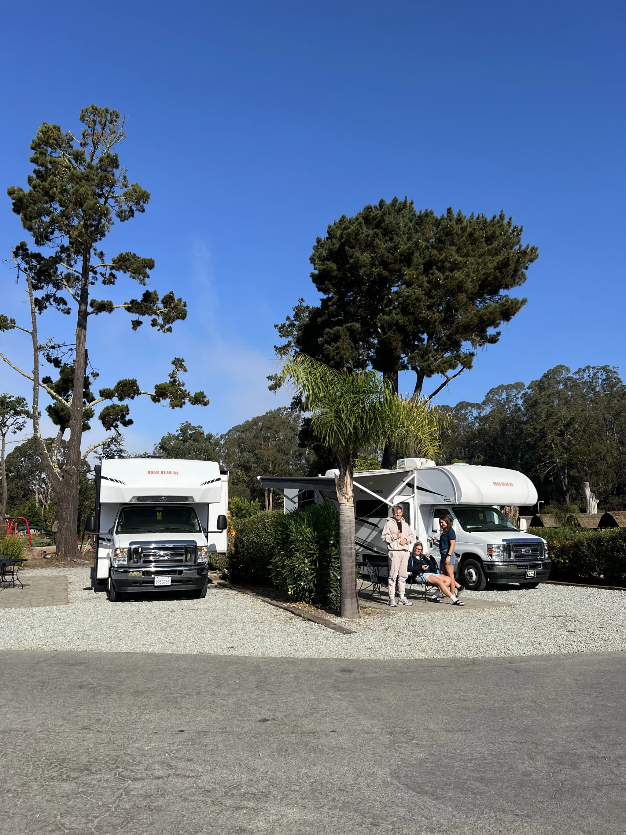 Zwei Camper am KOA Campground in Santa Cruz und drei junge Menschen die davor stehen und in die Kamera winken