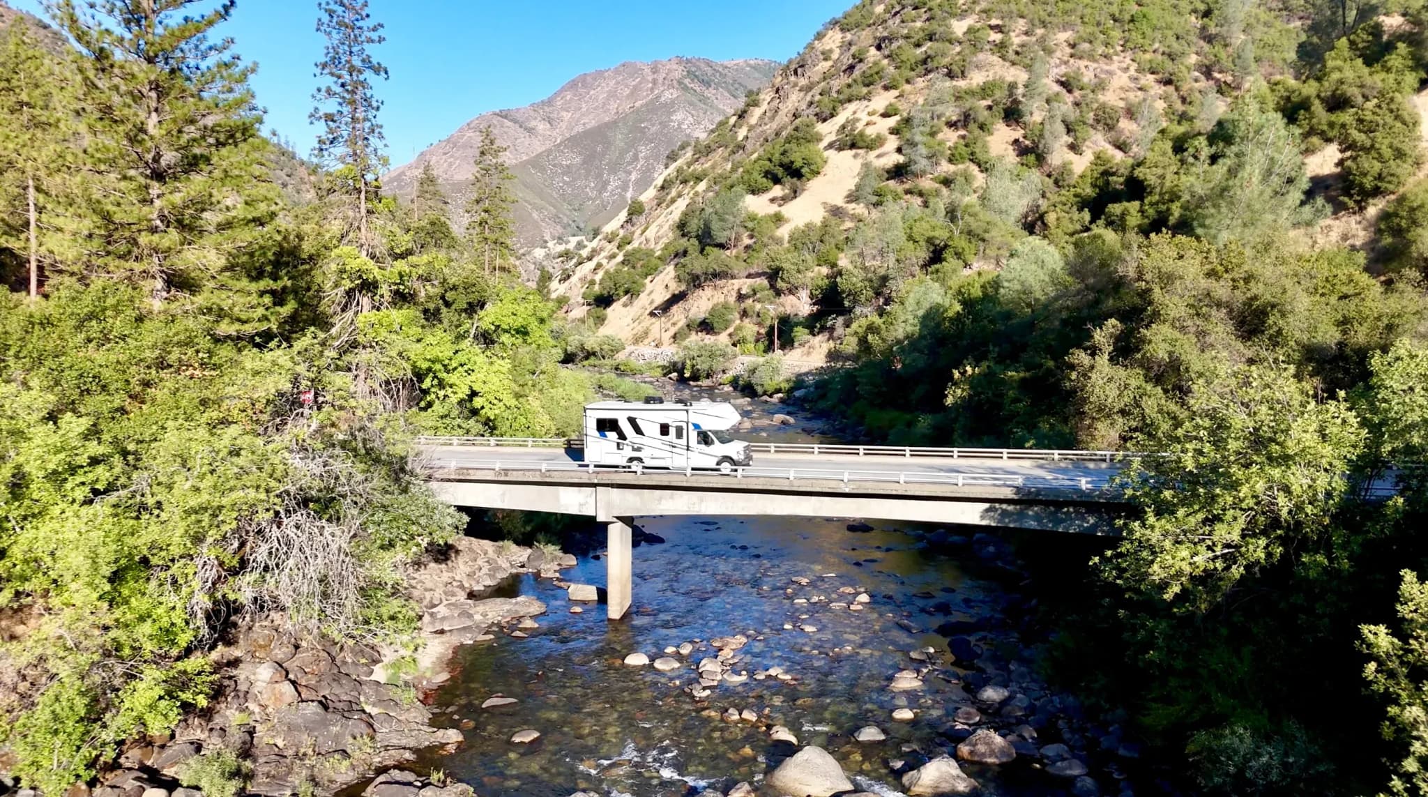 Wohnmobil auf einer Brücke im Yosemite National Park, umgeben von einem Fluss, dichten Wäldern und den Bergen der Sierra Nevada.