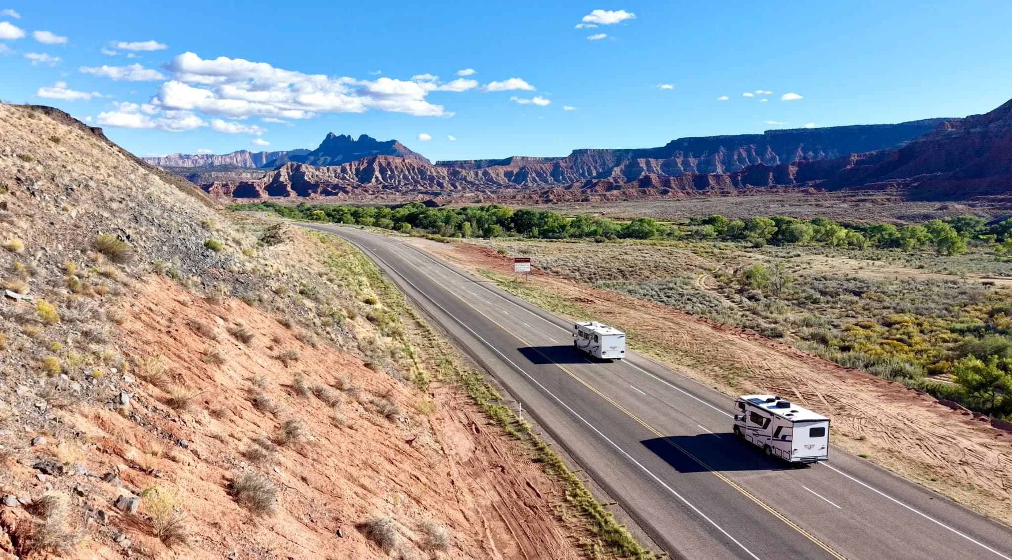 Zwei Wohnmobile fahren auf einer Straße durch die rote Felsenlandschaft am Eingang des Zion Nationalparks.