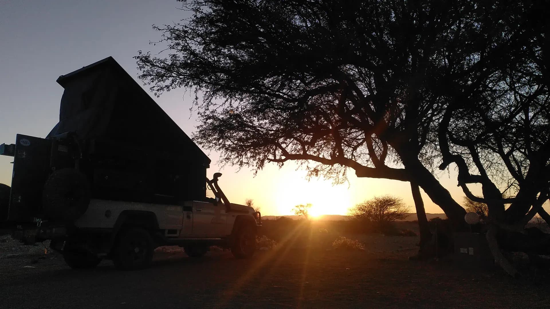 4WD Camper neben Baum in Namibia bei Sonnenuntergang