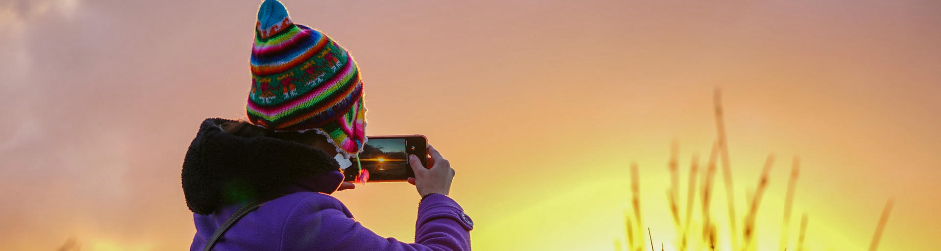 Frau mit bunter Mütze fotografiert Sonnenuntergang